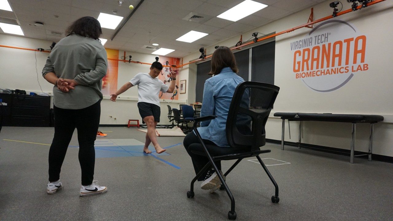 Image of a research participant performing a balance exercise while standing on a force plate and two researchers look on.