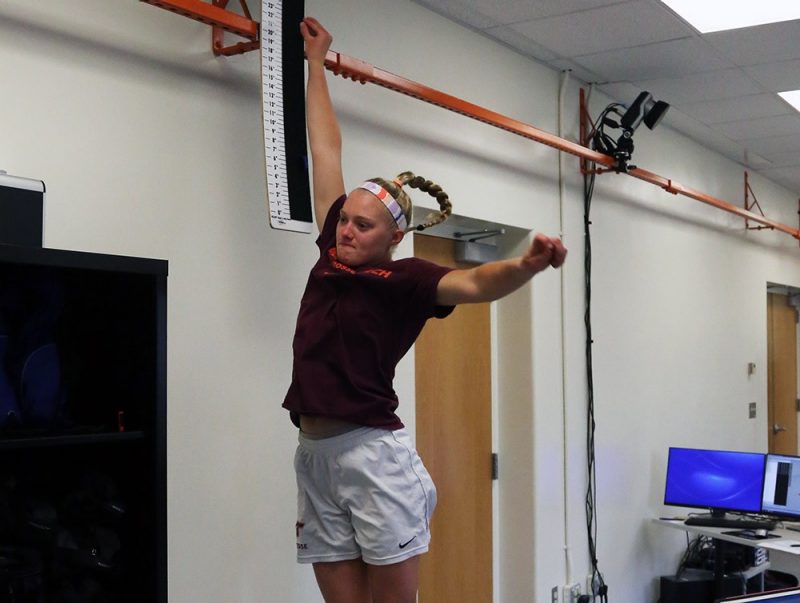 A female wearing a maroon shirt and white shorts performing a vertical jump.