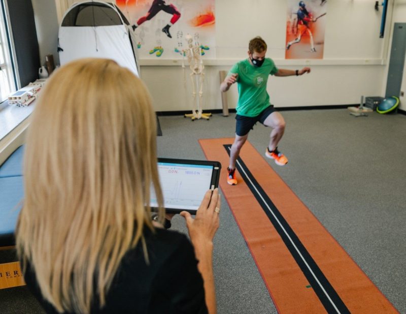 Participant hopping forward on one leg while wearing force sensing insoles. A researcher looks on while watching the data on an iPad.